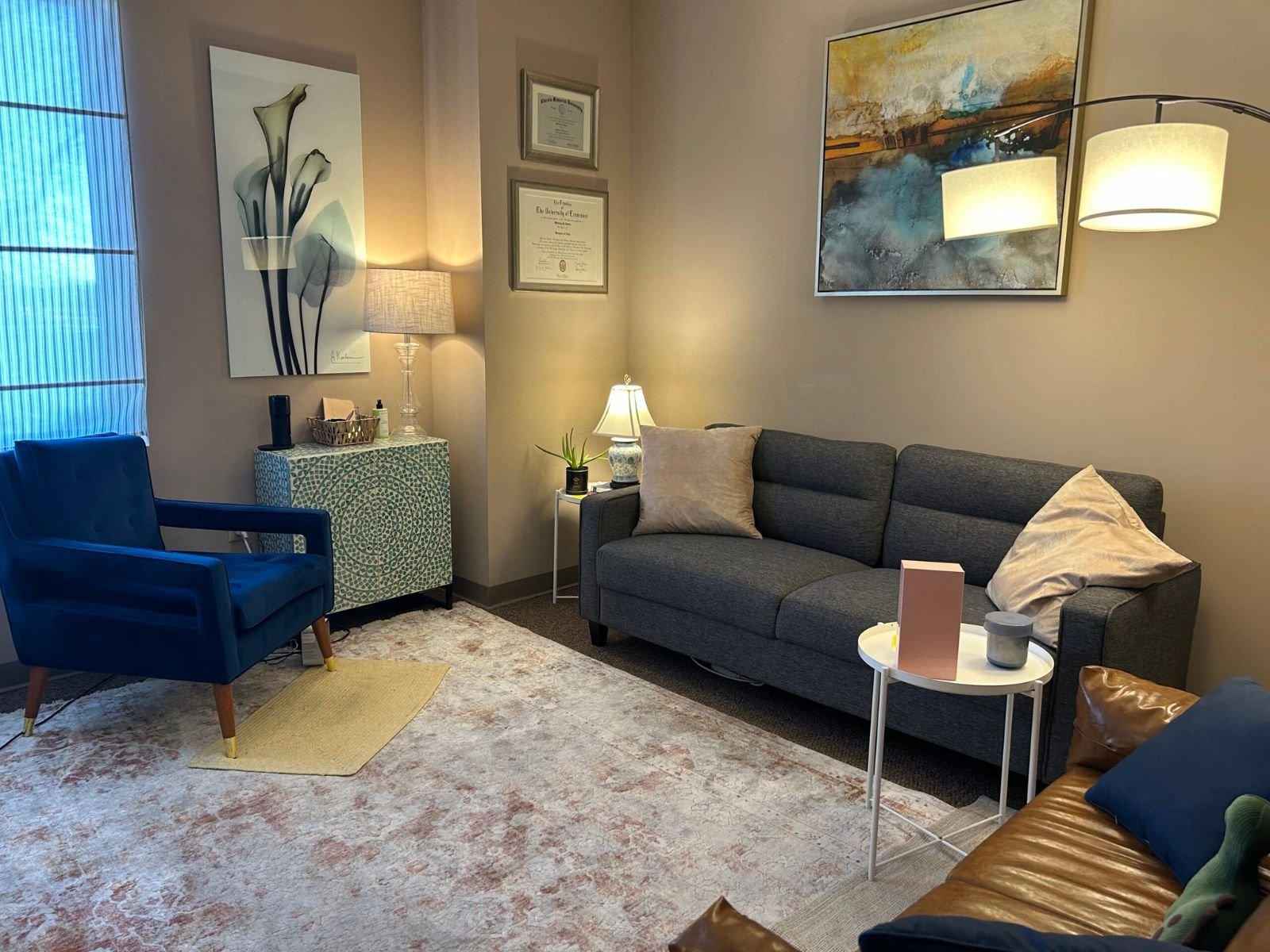 Another view of the office: blue armchair, gray sofa, lamps, and artwork